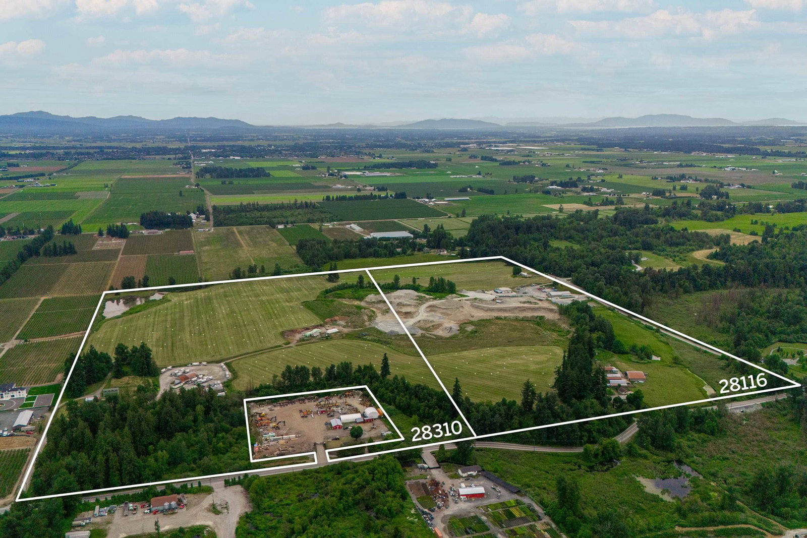 Aerial photograph of farmland in Abbotsford with two adjoining parcels outlined in white and labelled 28310 and 28116, with the Fraser Valley and mountains in the distance.